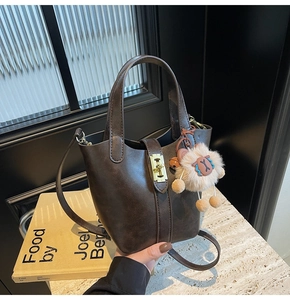 Detail of dark brown bucket bag with gold clasp and sheep charm on marble surface