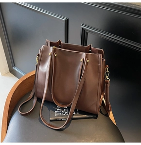 Detail of dark brown tote bag with metal rivets and detachable shoulder strap on chair