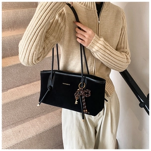 Detail of black suede tote bag with golden key charm and striped bow on long straps