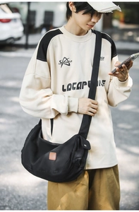 Outdoor-Streetstyle-Ansicht einer schwarzen Canvas-Umhängetasche mit breitem Gurt
