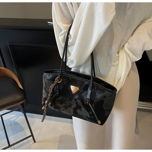 Détail d'un sac cabas en cuir verni plissé noir avec anneaux dorés et logo en métal