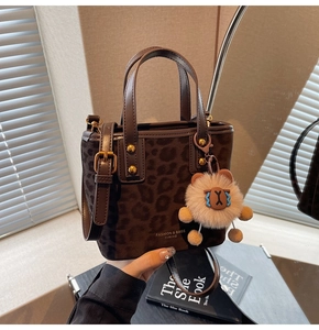 Detail of leopard print bucket bag with leather handles and plush animal keychain