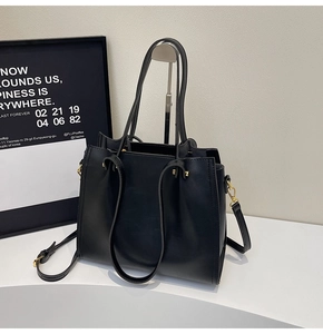 Detail of minimalist black leather tote bag with adjustable strap and golden hardware