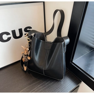Detail of black bucket bag featuring sleek synthetic leather and a cute bear charm
