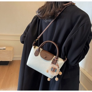 Detail view of a leather dumpling bag featuring a cute plush lamb charm and crossbody strap