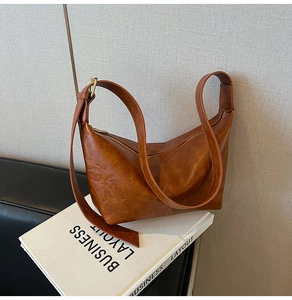 Close-up of brown vintage PU leather crescent bag on a white book with a textured wall