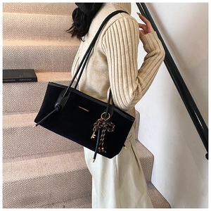 Detail of black suede tote bag with gold lettering and woven charm on beige stairs