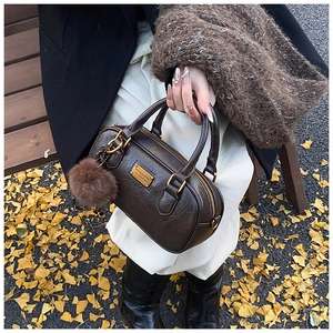 Close-up of brown Boston bag with lychee texture and a fluffy pom-pom charm