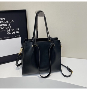 Detail of a black leather tote bag featuring gold hardware and adjustable shoulder strap