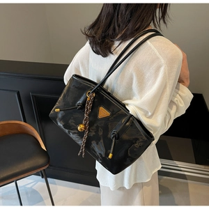 Détail d'un sac cabas en cuir verni noir avec logo triangle et pendentif boule en métal