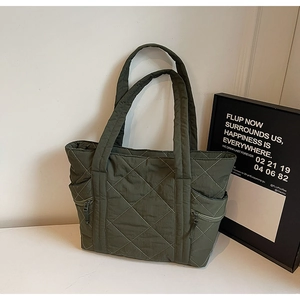 Detail of dark green quilted tote bag showing rhombus stitching and side zipper pocket