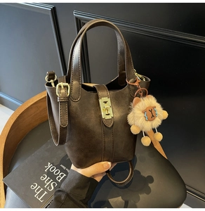 Detail of coffee brown bucket bag with gold clasp and plush lamb charm on dark wood background