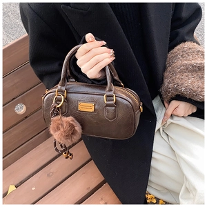 Detail view of a vintage dark brown Boston bag with golden hardware and fluffy pom pom charm