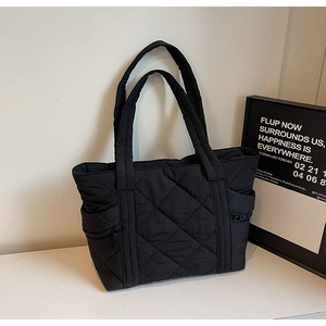Detail of black quilted tote bag showing puffer texture and side zipper pocket feature