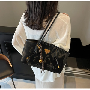 Détail du sac cabas noir brillant avec logo triangle en métal et pendentif clochette