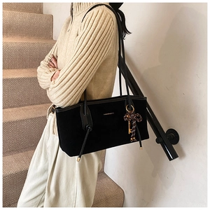 Detail of black velvet tote bag with golden lettering and bow key charm on a model