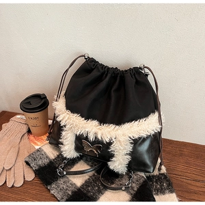 Detail view of a black leather drawstring bucket bag with white plush trim and metal butterfly