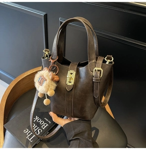 Close-up of a brown leather bucket bag with gold hardware and a cute furry charm.