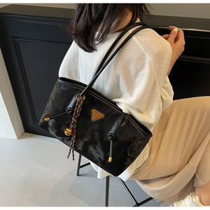 Détail d'un sac cabas noir avec logo triangle métallique et breloque cloche dorée décorative
