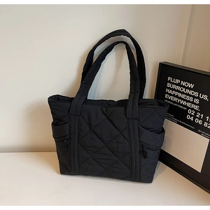 Detail view of the black quilted nylon tote bag showing side zipper pockets and texture