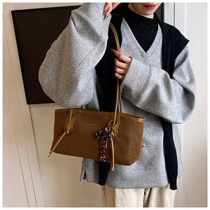 Detail view of brown matte tote bag with side braided knot and metal pendant accent