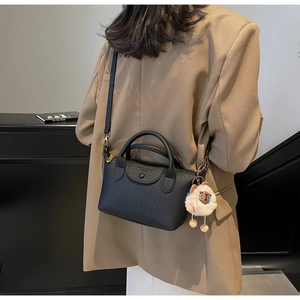 Detail of black lychee grain leather mini handbag with cute sheep pendant on a camel coat