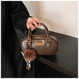Detailed view of brown Boston bag with textured leather and plush ball charm accessory