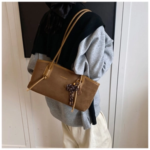 Detail of a brown suede tote bag with a striped bow and tennis racket charm pendant