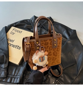 Detail of leopard print bucket bag with plush charm and leather handle on a black jacket