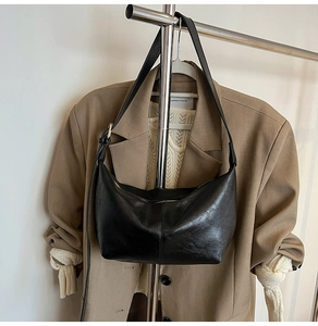 Detail of a black crescent shoulder bag in glossy leather shown with a brown blazer