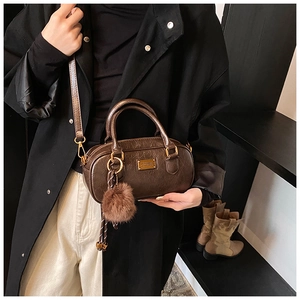 Detail of dark brown leather Boston bag with gold metal plate and faux fur pompom charm