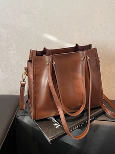 Brown leather tote bag with double handles and shoulder strap shown in a modern studio setting