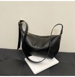 Detail view of black oiled leather crescent bag with adjustable strap on a bench