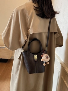 Dark brown leather bucket bag with gold lock and plush sheep charm on a trench coat model