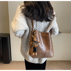 Brown leather bucket bag with a cute rabbit plush charm shown in a cozy lifestyle shot