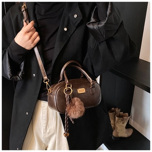 Detail of dark brown retro Boston bag with gold metal logo and plush ball keychain charm