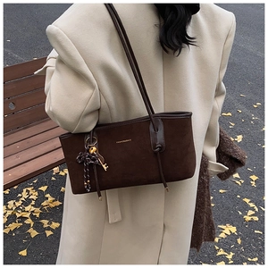 Detail of dark brown suede tote bag with golden lettering and bow charm outdoors