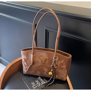 Détail du sac cabas marron brillant avec plaque dorée et pendentif clochette de luxe