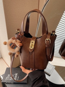 Dark brown leather bucket bag with gold lock and lion charm on fashion book background