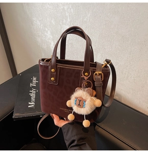 Detail of dark brown leopard embossed bucket bag with gold hardware and plush sheep charm