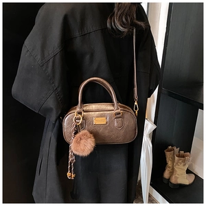 Detail of coffee brown Boston bag with plush ball charm and oil-wax leather texture