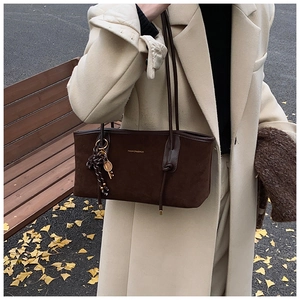 Close-up of a dark brown matte tote bag with a golden logo and metal pendant