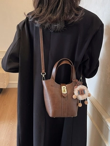 Vintage brown PU leather bucket bag with metal lock and plush charm worn by model