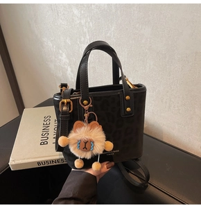 Detail of leopard print handbag featuring a plush bear charm and metallic brand lettering