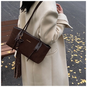Brown suede tote bag with ribbon detail shown in an autumn street scene with fallen leaves