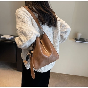 Detail view of brown leather bucket bag with cute rabbit pendant and wide shoulder strap