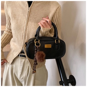 Detail of black Boston bag with gold nameplate and fluffy brown pompom charm