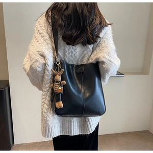Detail of vintage black bucket bag with rabbit charm worn over a white sweater