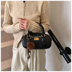 Woman carrying a black Boston bag with a vintage texture and a brown plush charm