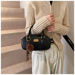 Detail of black textured Boston bag with gold hardware and brown faux fur charm